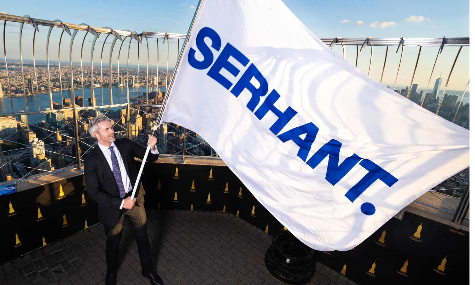 Ryan Serhant holding a SERHANT. flag above New York City